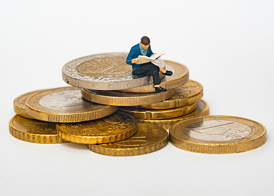 man sitting on coins reading a book